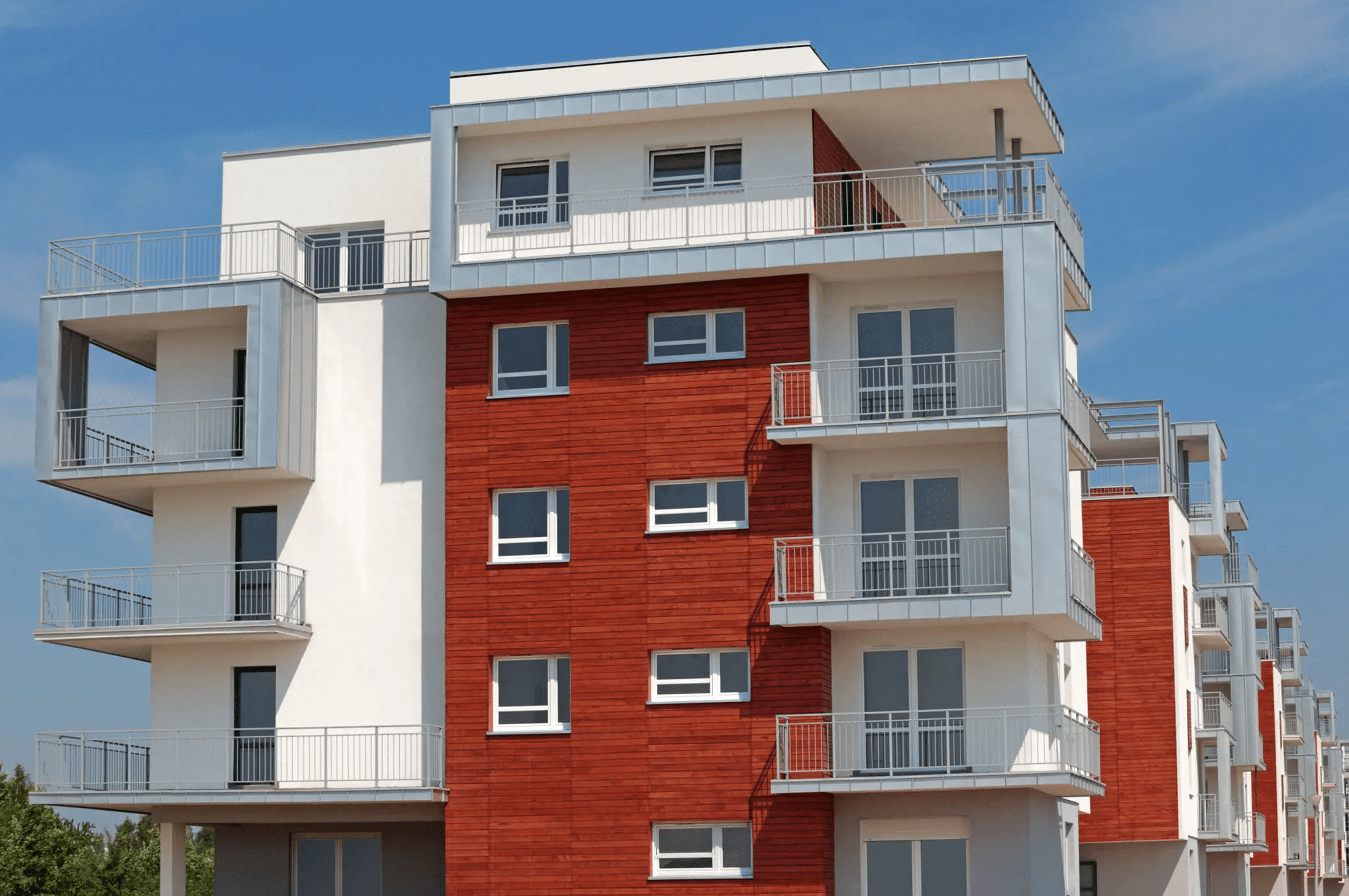 Modern apartment building with white and red exterior and multiple balconies under a clear blue sky.